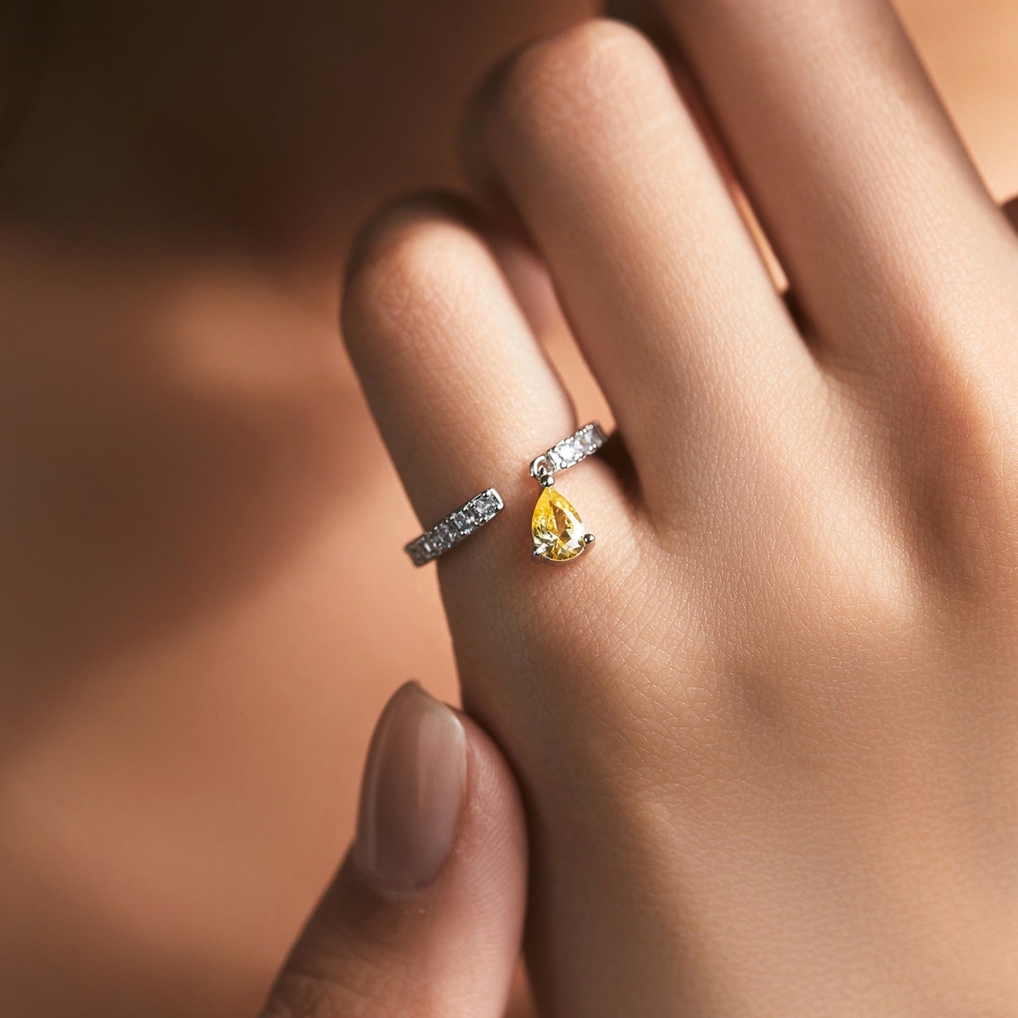 Adjustable sterling silver ring with yellow cubic zirconia droplet being worn on a finger.