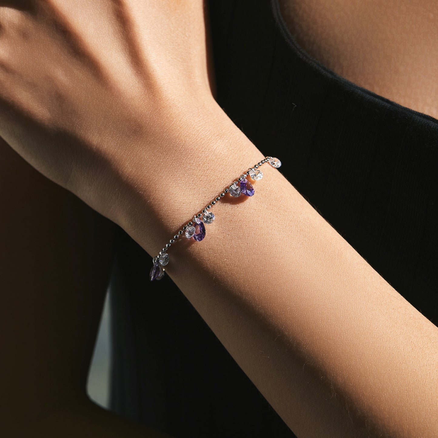 Sterling silver bracelet with purple and clear cubic zirconia droplets being worn.