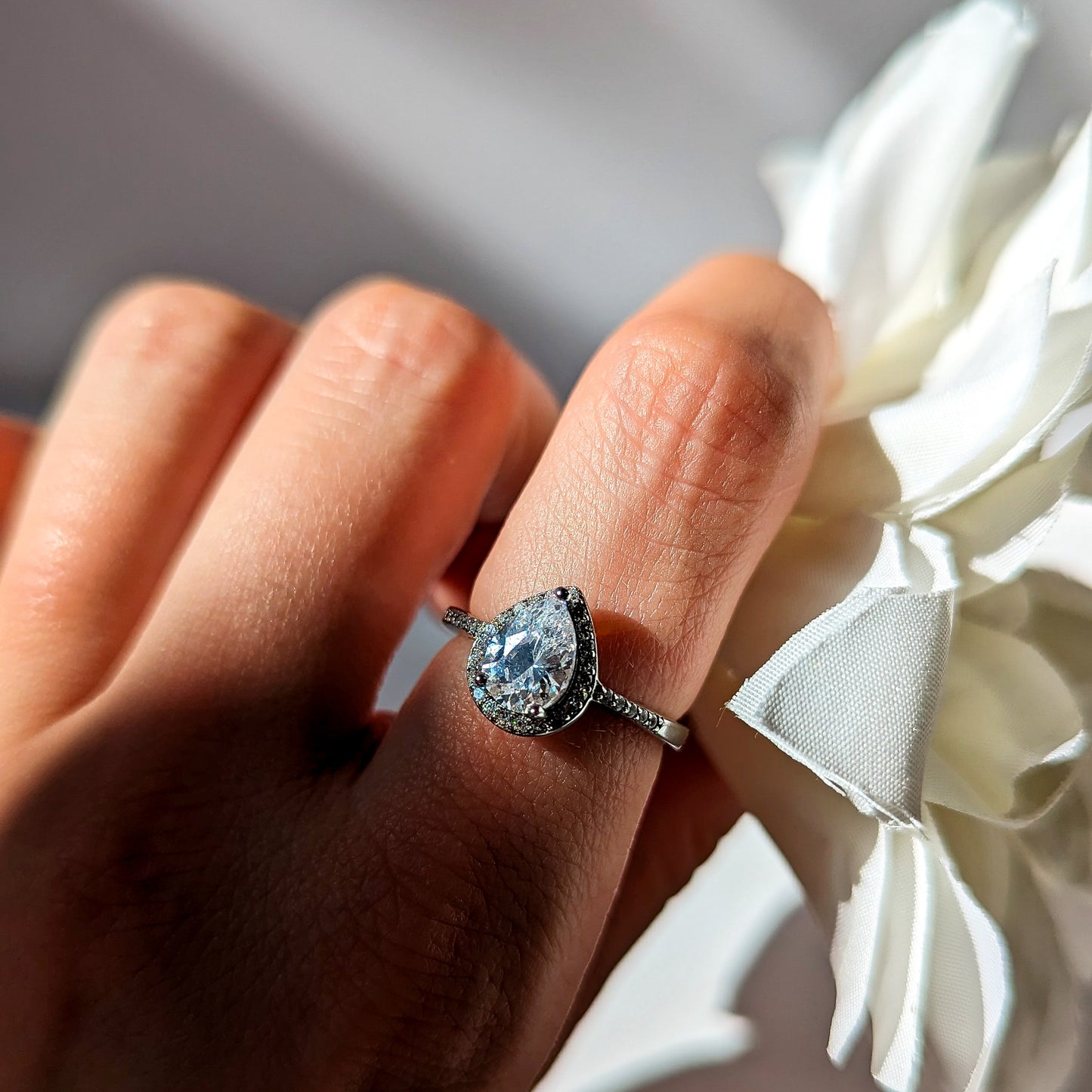 Model hand showcasing silver ring with pear-shaped central gem and surrounding sparkly stones