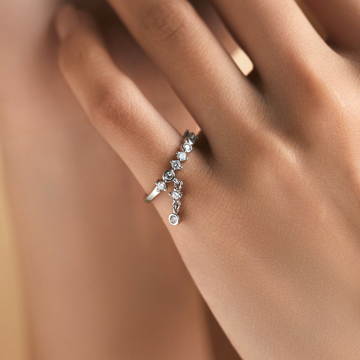 Elegant sterling silver ring with sparkling cubic zirconias and tassel charm, styled on model.