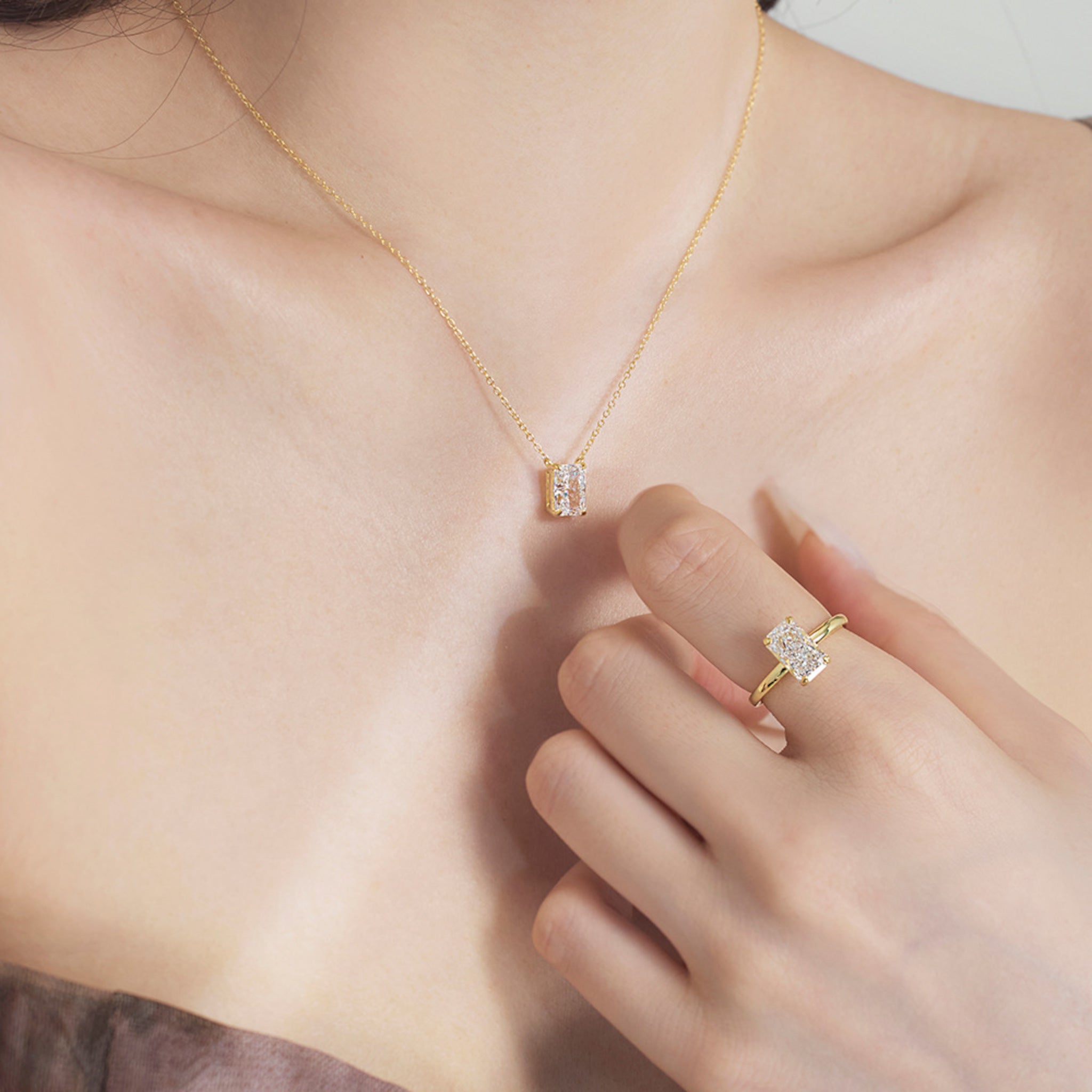 Gold ring and necklace with matching clear cubic zirconia pendants, worn for a cohesive look.