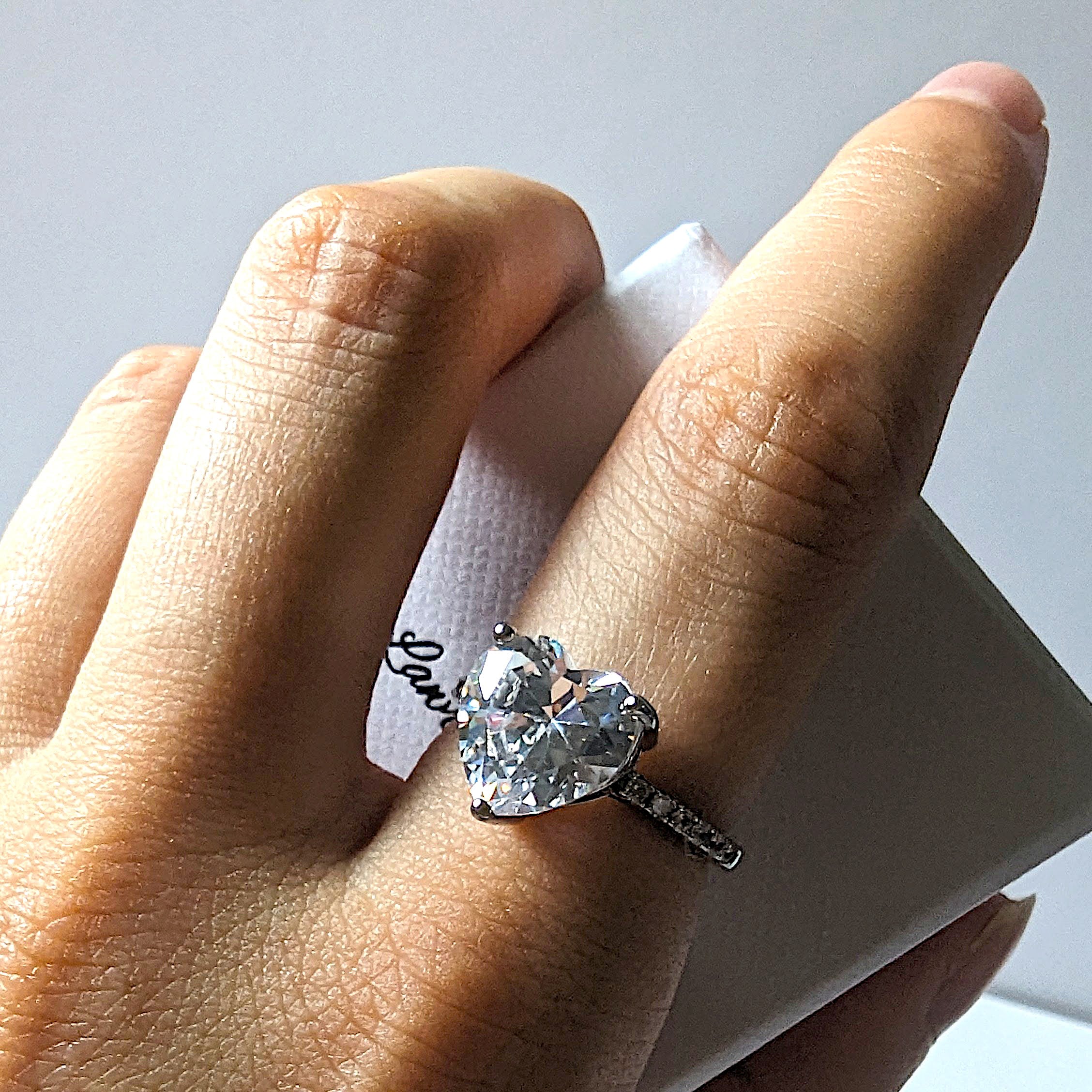 Model wearing silver ring with sparkling heart shaped gemstone. 